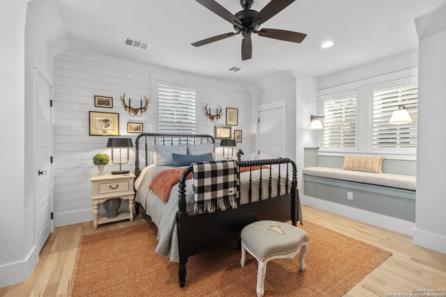 bedroom featuring light hardwood / wood-style floors, multiple windows, wooden walls, and ceiling fan