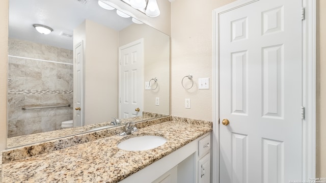 bathroom with toilet, vanity, and tiled shower