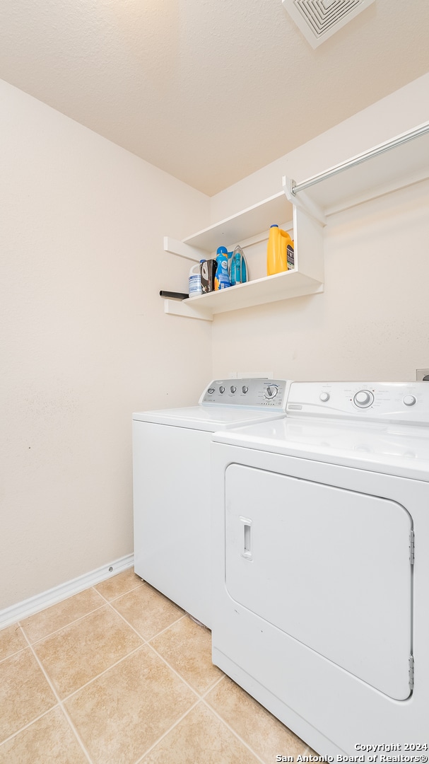 clothes washing area with washing machine and clothes dryer and light tile patterned floors