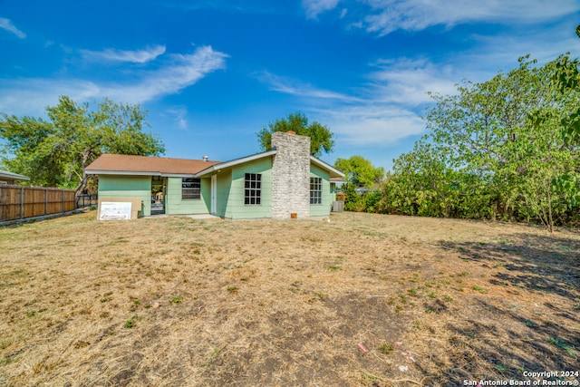 back of property featuring a garage, a chimney, fence, and a lawn