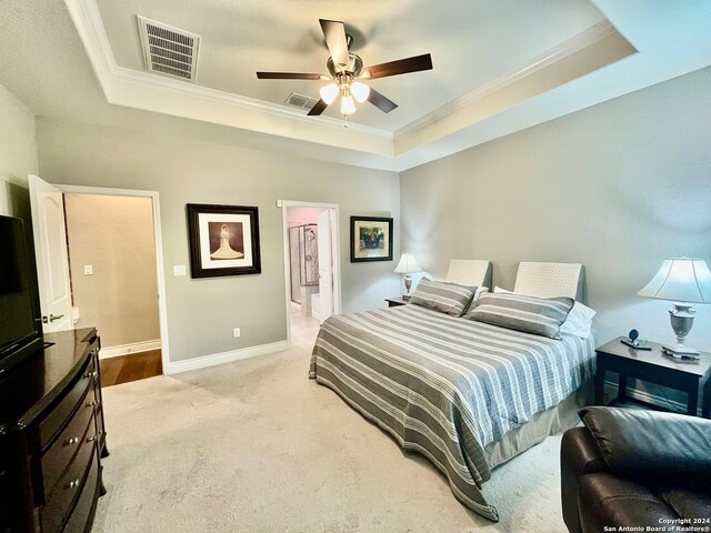 bedroom featuring a tray ceiling, ceiling fan, light carpet, connected bathroom, and crown molding