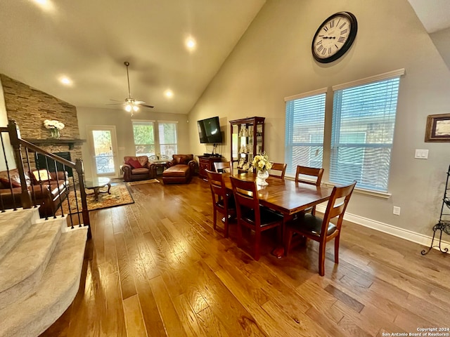 dining area with high vaulted ceiling, wood-type flooring, a fireplace, and ceiling fan