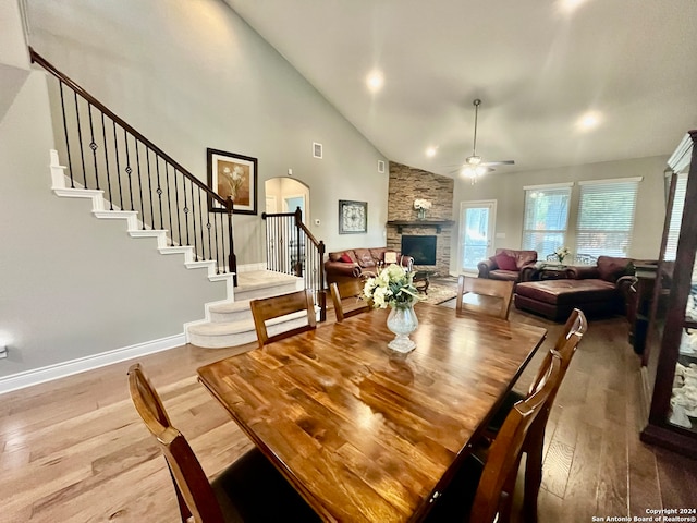 dining space with hardwood / wood-style floors, a fireplace, high vaulted ceiling, and ceiling fan