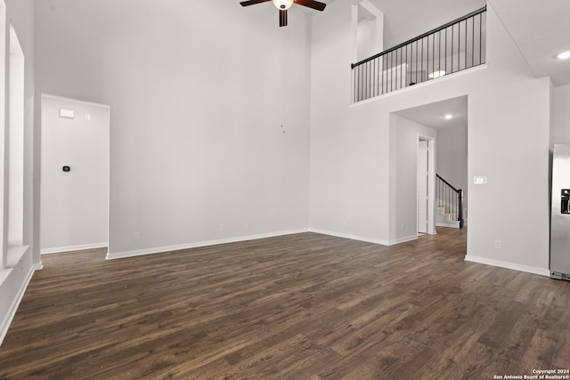 unfurnished living room featuring ceiling fan, a towering ceiling, and dark wood-type flooring