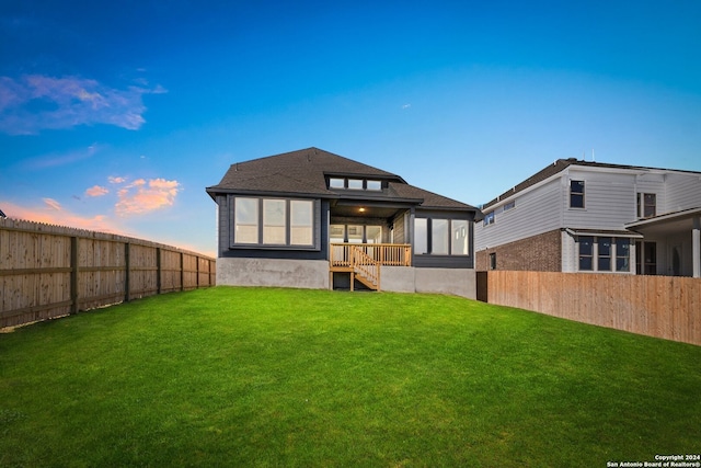 back house at dusk featuring a lawn