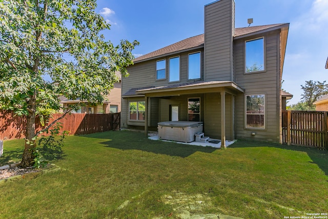 rear view of property with a hot tub and a lawn