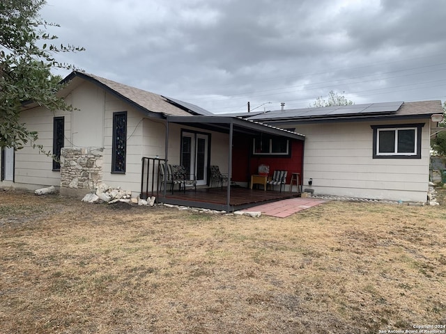 back of property with roof mounted solar panels and a yard