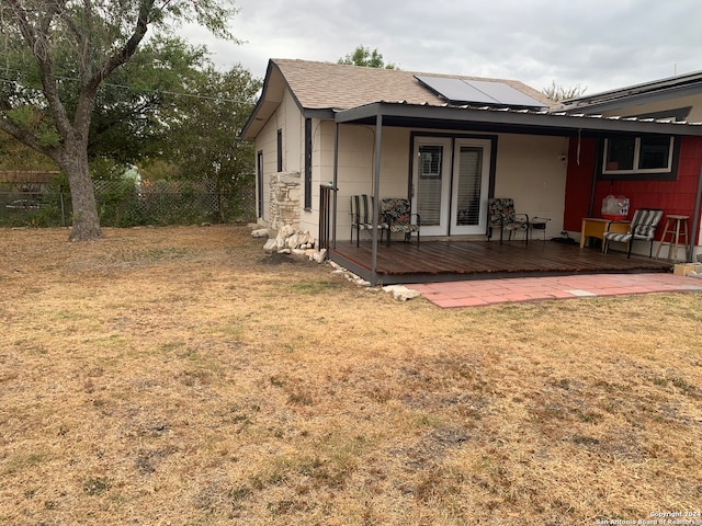 rear view of property featuring a yard, a deck, and solar panels