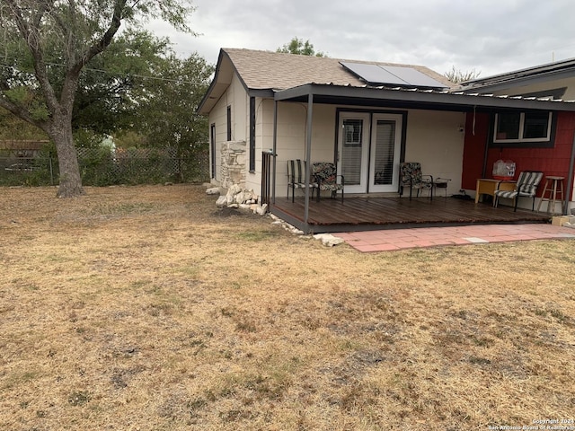 back of property with roof mounted solar panels, a lawn, fence, and a deck