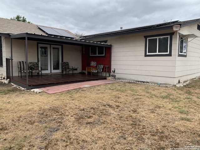 rear view of property with roof mounted solar panels, a yard, and a deck