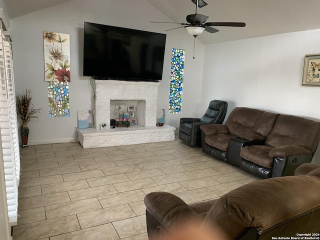 living room featuring light tile patterned flooring, lofted ceiling, a ceiling fan, and a stone fireplace