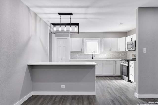 kitchen with appliances with stainless steel finishes, dark hardwood / wood-style flooring, kitchen peninsula, decorative light fixtures, and white cabinets