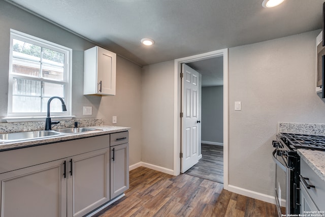 kitchen with light stone countertops, sink, white cabinets, gas range, and dark hardwood / wood-style floors