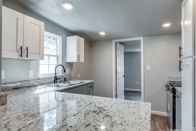 kitchen featuring light stone countertops, sink, dark hardwood / wood-style flooring, white cabinetry, and stainless steel gas range