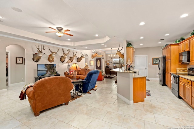 kitchen featuring black appliances, sink, ceiling fan with notable chandelier, a breakfast bar, and a kitchen island with sink