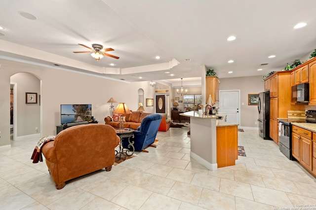 kitchen featuring an island with sink, a breakfast bar, black appliances, ceiling fan with notable chandelier, and sink