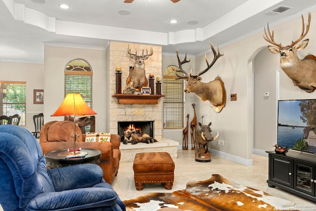 tiled living room with crown molding, a stone fireplace, and ceiling fan