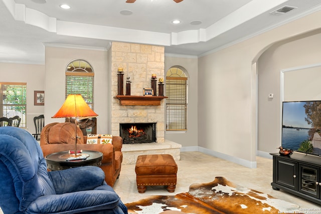 living room featuring crown molding, light tile patterned flooring, a stone fireplace, and ceiling fan