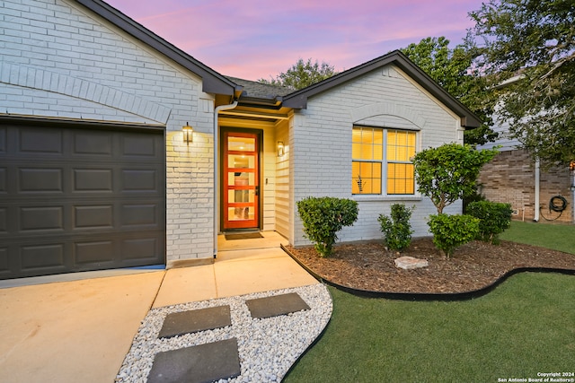 exterior entry at dusk featuring a lawn and a garage