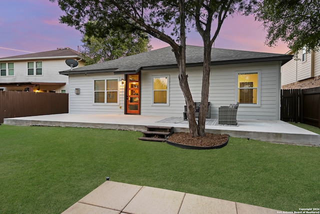 back house at dusk with a patio area and a lawn