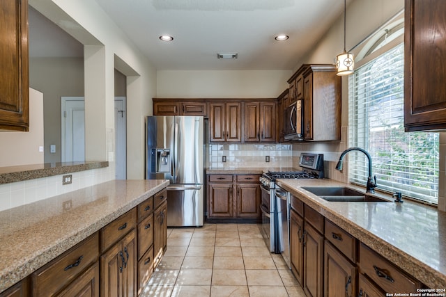 kitchen with appliances with stainless steel finishes, light tile patterned flooring, sink, pendant lighting, and light stone counters