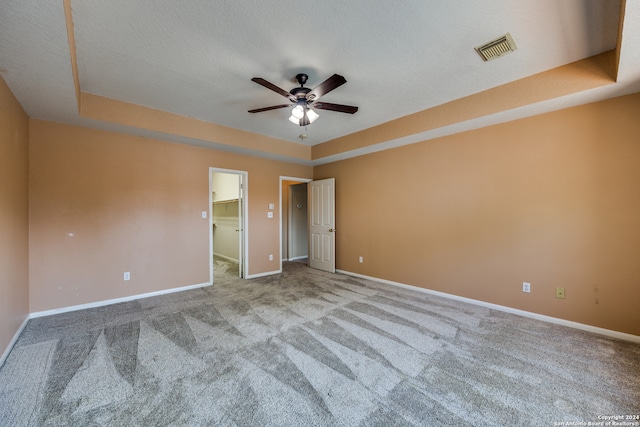 carpeted spare room featuring a textured ceiling, a tray ceiling, and ceiling fan