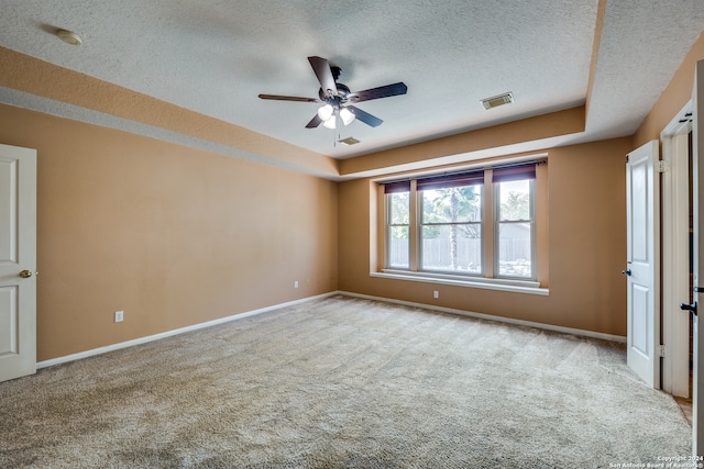 unfurnished bedroom featuring a raised ceiling, a textured ceiling, light colored carpet, and ceiling fan