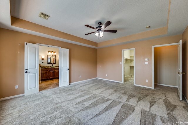 unfurnished bedroom with a spacious closet, a tray ceiling, a closet, ceiling fan, and light carpet