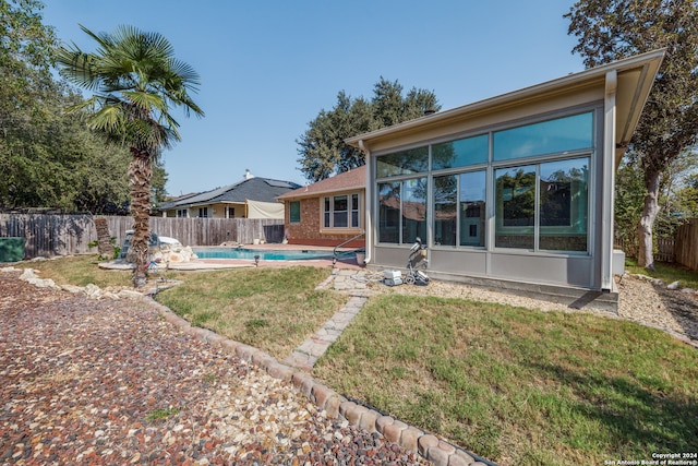 back of house featuring a sunroom, a fenced in pool, and a lawn