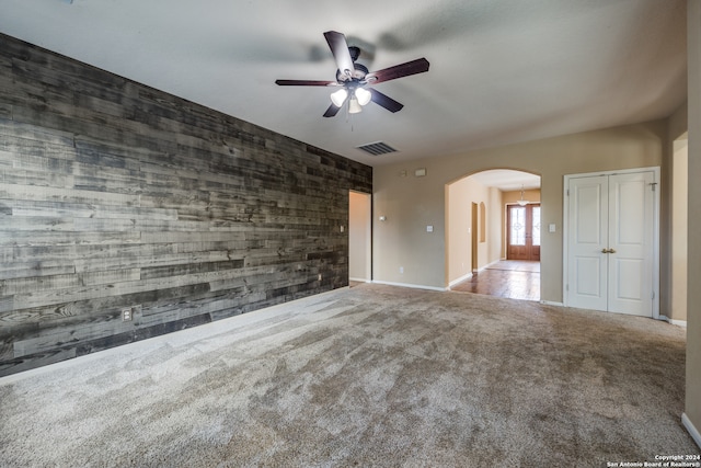 spare room featuring ceiling fan, wood walls, and light carpet