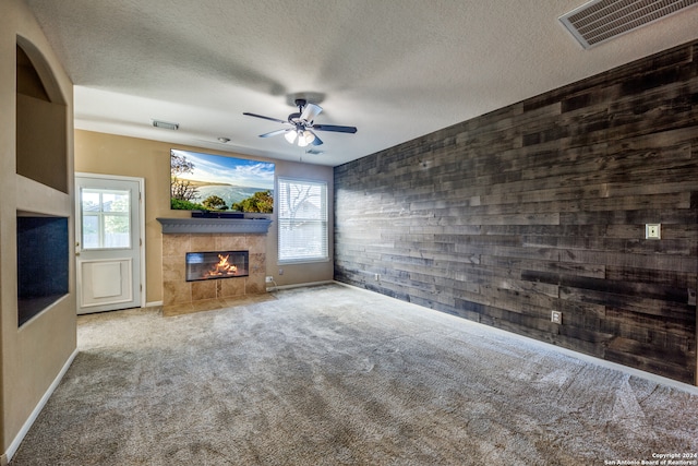 unfurnished living room featuring light carpet, a tiled fireplace, ceiling fan, a textured ceiling, and wood walls