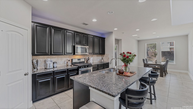 kitchen featuring a center island with sink, sink, a breakfast bar, appliances with stainless steel finishes, and tasteful backsplash