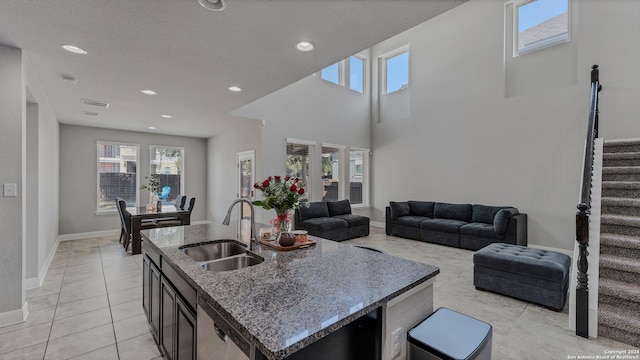 kitchen featuring plenty of natural light, a towering ceiling, sink, and an island with sink