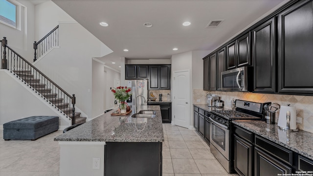 kitchen featuring stainless steel appliances, decorative backsplash, sink, and an island with sink