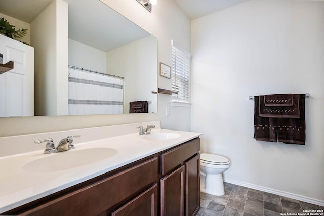 full bath featuring baseboards, toilet, a sink, and double vanity
