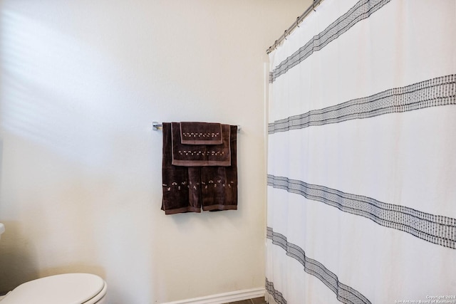 full bath featuring toilet, a shower with shower curtain, and baseboards