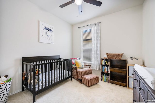 bedroom with light colored carpet, ceiling fan, and a nursery area