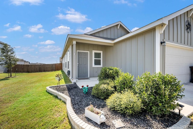 property entrance featuring driveway, board and batten siding, fence, a yard, and a garage