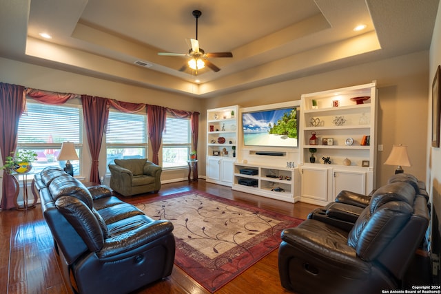 living room featuring dark wood-type flooring, ceiling fan, and a raised ceiling