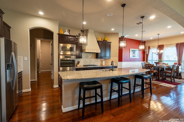 kitchen with a kitchen island with sink, dark hardwood / wood-style floors, appliances with stainless steel finishes, sink, and premium range hood