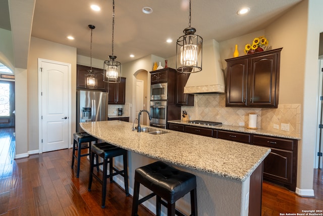 kitchen with a kitchen island with sink, dark brown cabinets, sink, appliances with stainless steel finishes, and dark hardwood / wood-style flooring