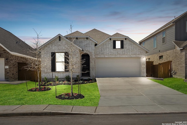 french country style house with driveway, an attached garage, a front yard, and brick siding