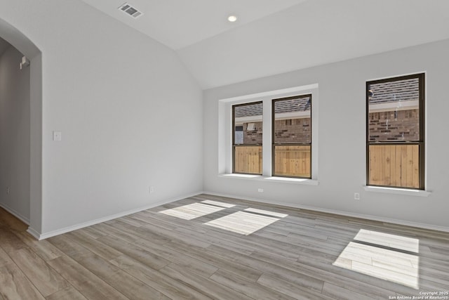 unfurnished room with lofted ceiling, visible vents, baseboards, arched walkways, and light wood finished floors