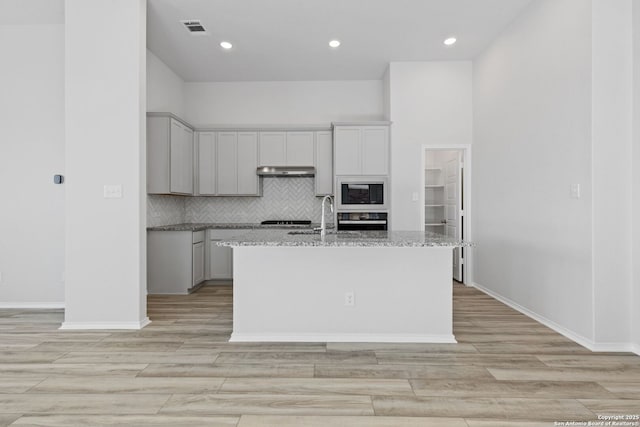 kitchen with light wood-type flooring, tasteful backsplash, black appliances, visible vents, and an island with sink