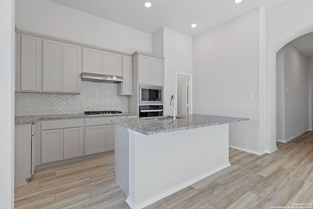 kitchen with arched walkways, light stone counters, appliances with stainless steel finishes, backsplash, and a sink