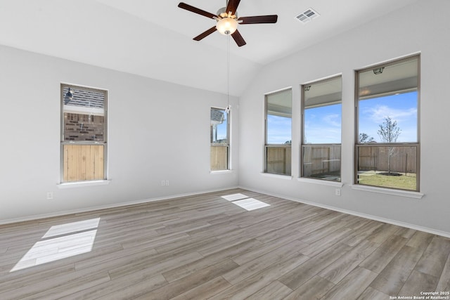 empty room featuring lofted ceiling, light wood-style floors, ceiling fan, visible vents, and baseboards