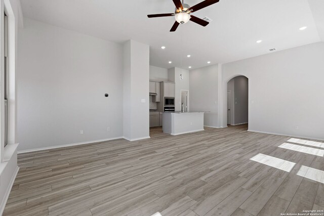 unfurnished living room featuring baseboards, arched walkways, recessed lighting, light wood finished floors, and a ceiling fan