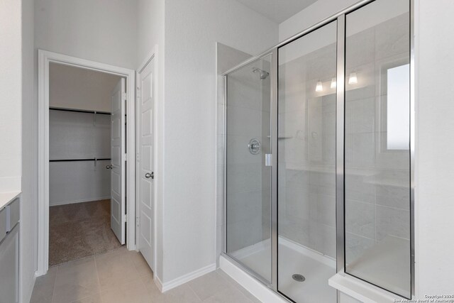 full bath featuring a spacious closet, a shower stall, baseboards, vanity, and tile patterned flooring
