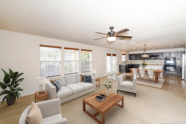 carpeted living room with a textured ceiling, sink, and ceiling fan