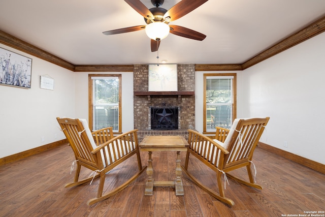 living area featuring hardwood / wood-style floors, a brick fireplace, crown molding, and ceiling fan